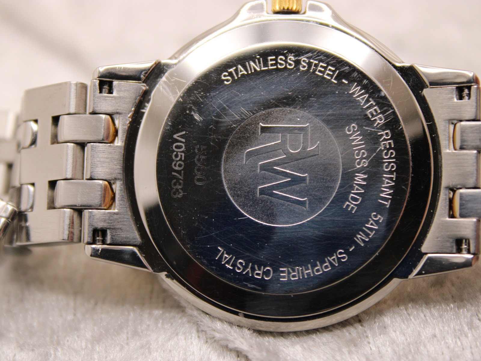 Close-up of the stainless steel case back, showing Raymond Weil logo, serial V059733, model 5560, 'Swiss Made', 'Water Resistant 5ATM', and 'Sapphire Crystal' engravings.
