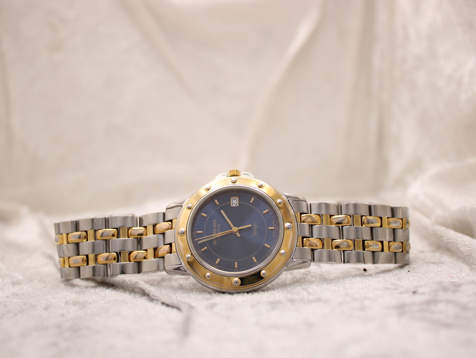 Full front view of the Raymond Weil Tango watch with its two-tone bracelet laid flat on a light textured surface.