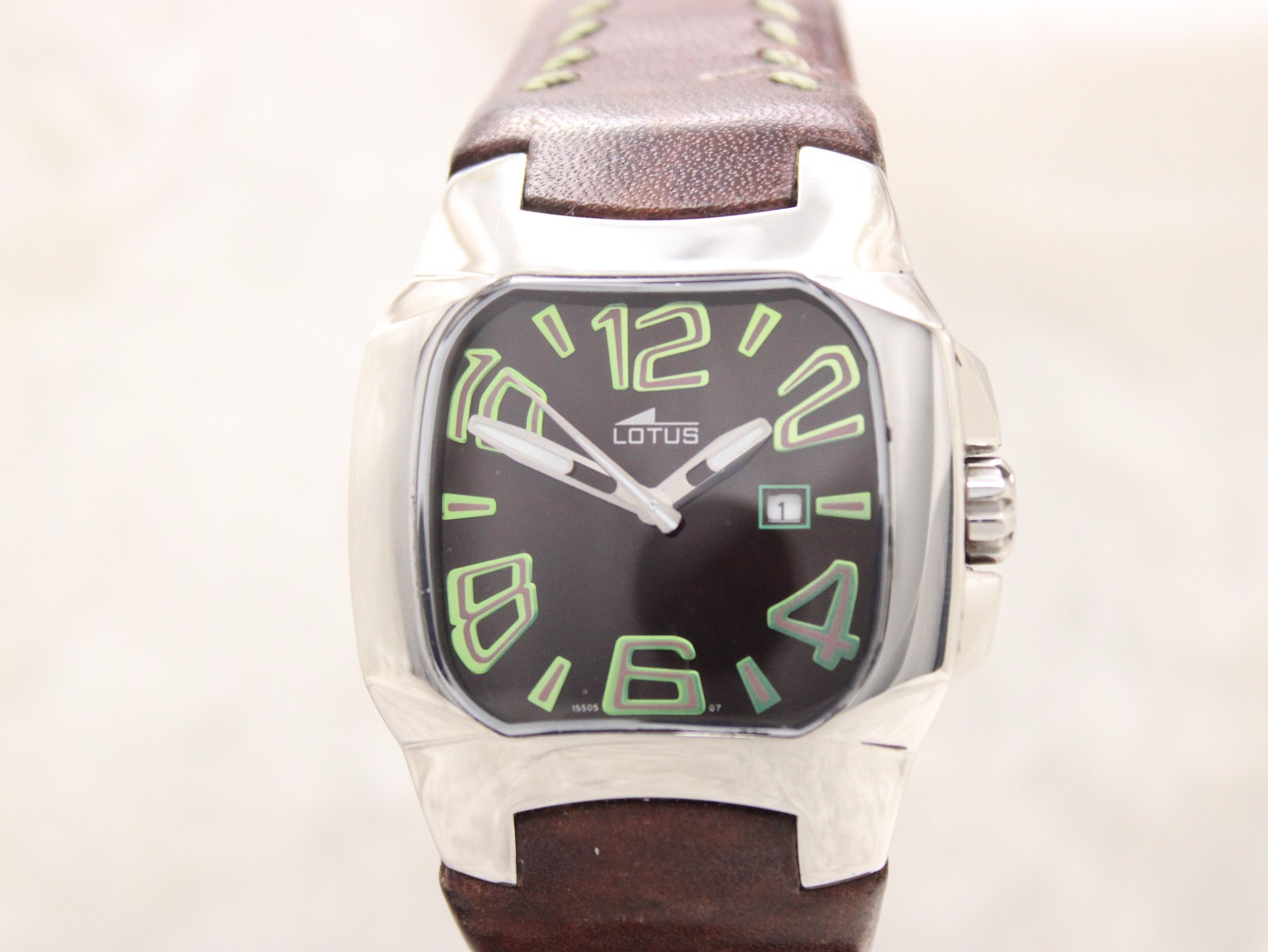 Close-up front view of the Lotus 15509 black dial with luminous green Arabic numerals, white hands, and date window, highlighting the texture of the brown leather strap.