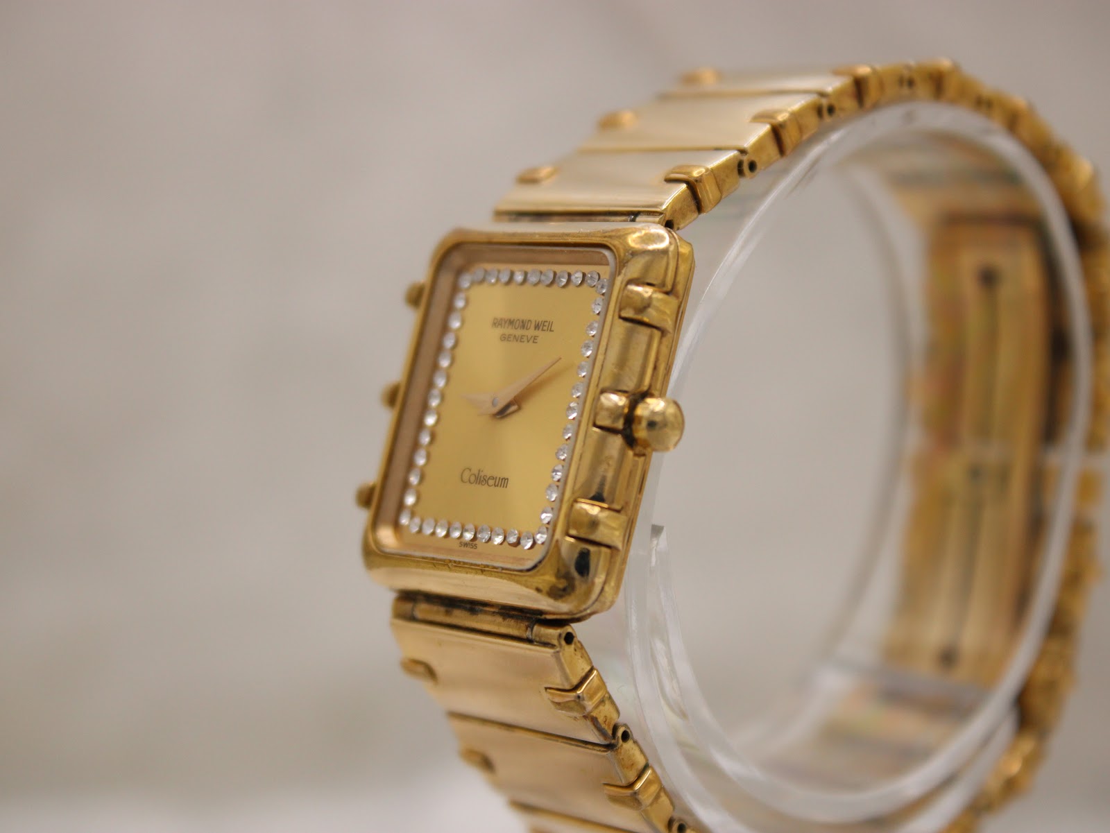 Angled view of the Raymond Weil Coliseum on a display stand, showing the rectangular gold case and bracelet.