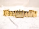 Full front view of the gold-plated Raymond Weil Coliseum watch with bracelet extended on a white textured surface.