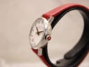 Side profile of the Mondaine watch, highlighting the polished stainless steel case and the distinctive red-crowned winder.