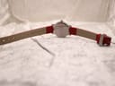 Full back view of the Mondaine watch with the red leather strap fully extended, clearly showing the case back and "GENUINE LEATHER" embossed on the strap.