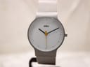 Front view of a Braun BN0211 watch with a white dial and silver-grey matte case on a watch stand, showing the yellow seconds hand.