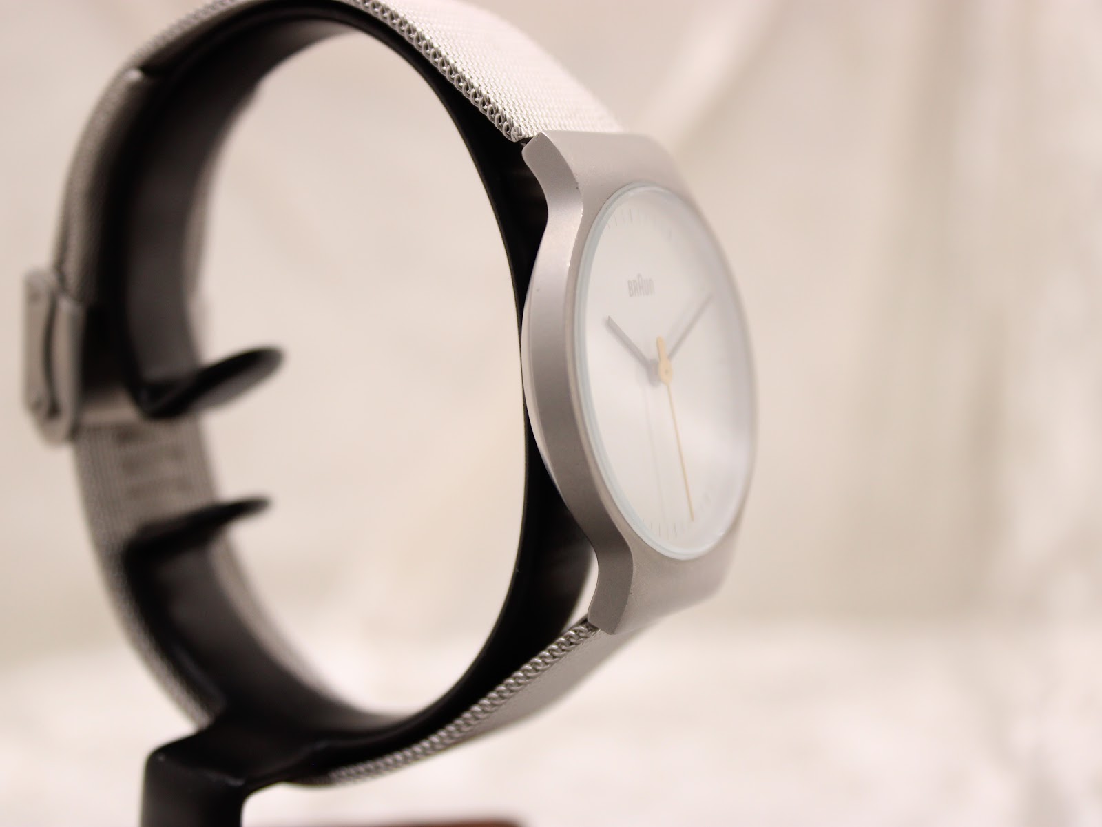 Angled side view of the Braun BN0211 watch, highlighting the minimalist white dial and the textured stainless steel mesh bracelet.