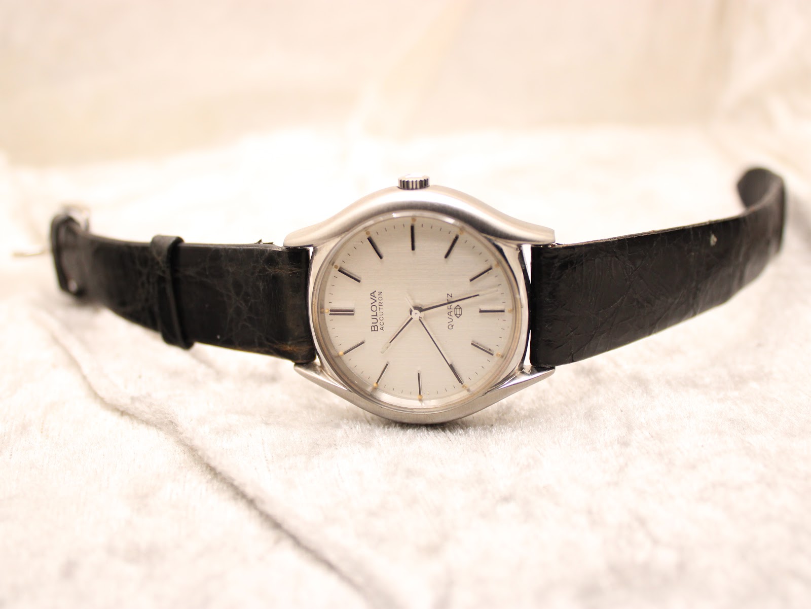 Full front view of the Bulova Accutron watch laid flat, displaying the silver dial and black leather strap.