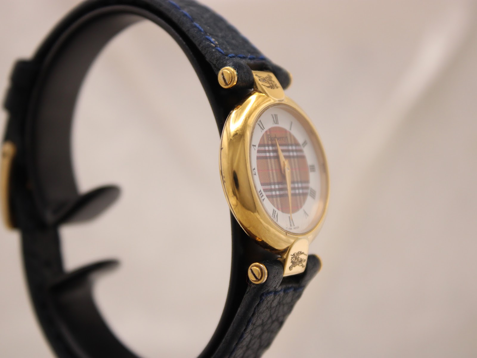 Angled view of the Burberrys watch highlighting the gold-tone case and blue strap.