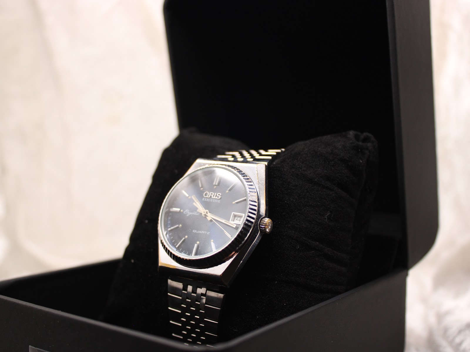 Angled view of the Oris Executive Crystal watch nestled in a black display box cushion.