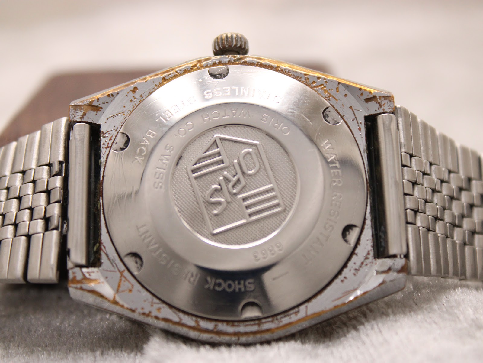 Rear view of the watch, showing the stainless steel case back with Oris logo and "water resistant" text, alongside plating wear.