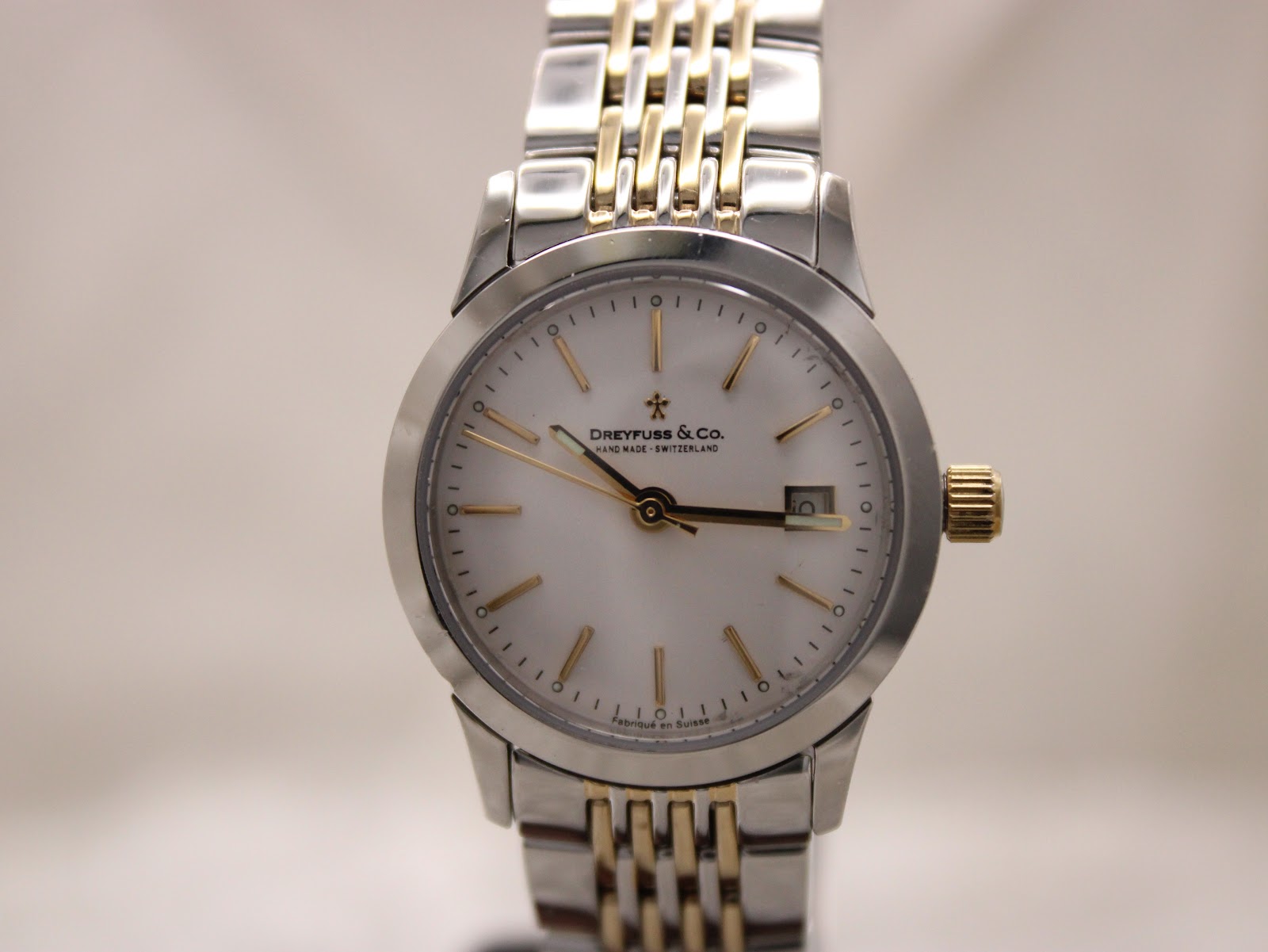 Straight-on front view of the Dreyfuss & Co white dial with gold baton hour markers and a date window at 3 o’clock.