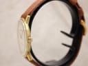 Side profile of the Roamer watch, showing the slim gold-tone case, domed acrylic crystal, and the signed Roamer crown.
