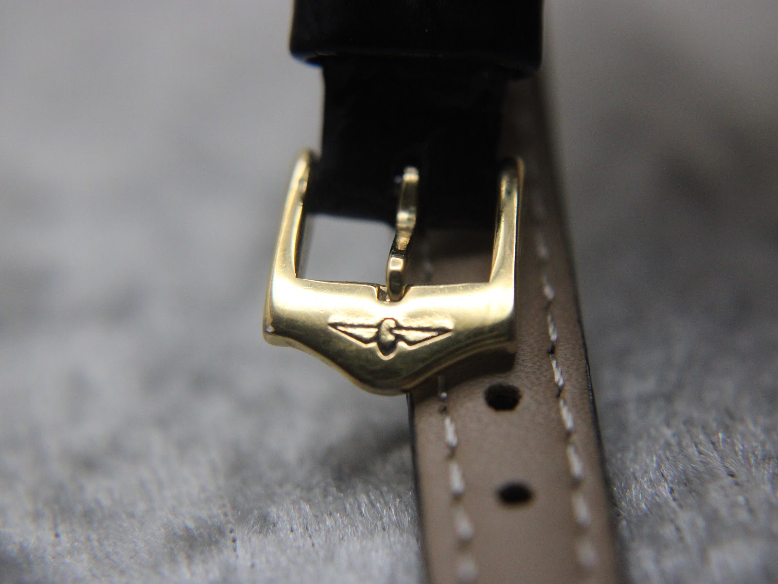 Detailed close-up of the gold-tone buckle on the black leather strap, featuring the distinct Rotary wing logo engraving.