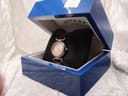 The Rotary watch presented inside its original blue hinged box, resting on a black cushion, with a small white price tag visible in the background.