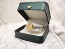 The watch presented in an open dark green watch box with a gold crown emblem on the lid.