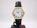 Front view of the Raymond Weil Genève 9140 watch, showing its gold electroplated case, white Roman numeral dial, and black leather strap on a stand.