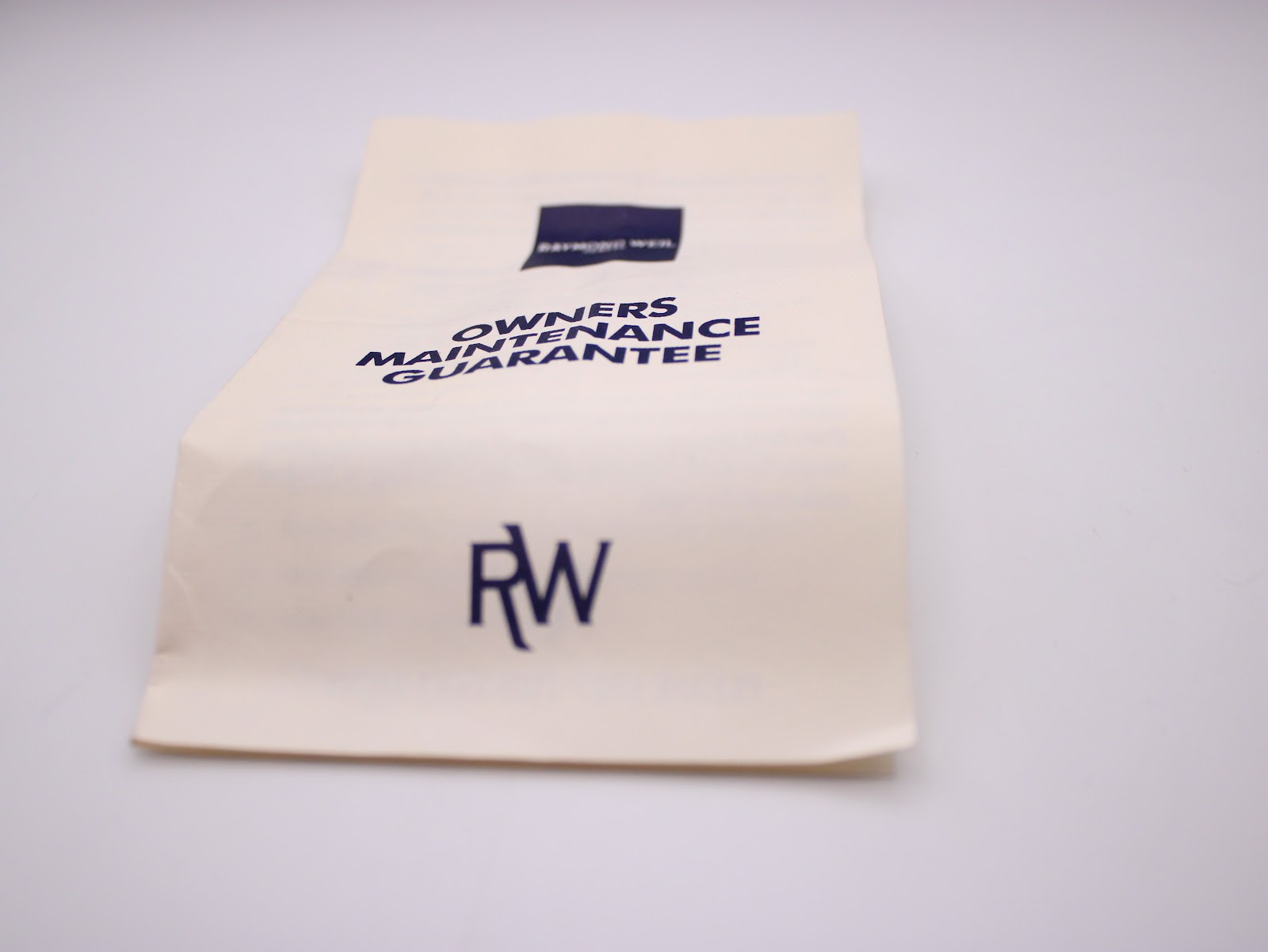 Close-up of the Raymond Weil Owners Maintenance Guarantee booklet on a white background.