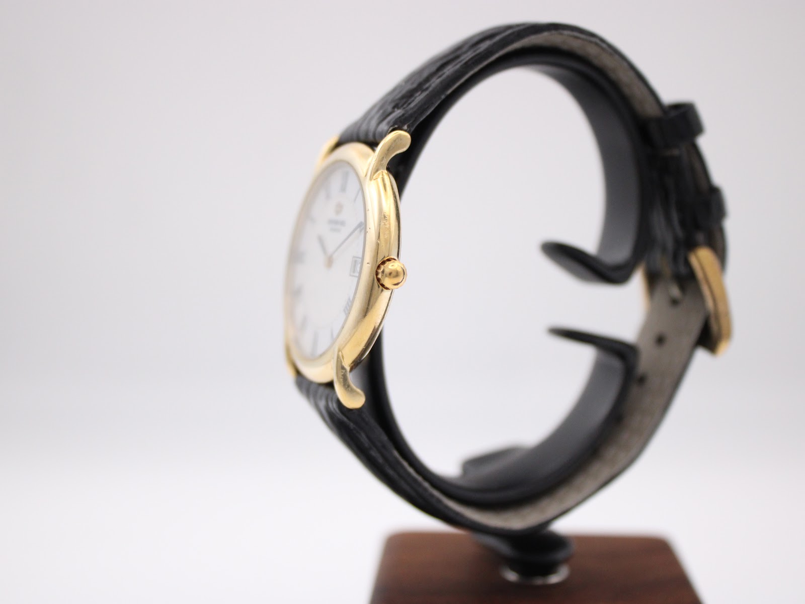 Side profile view of the Raymond Weil watch on a stand, highlighting the gold-tone crown and the curvature of the case.