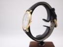 Side profile view of the Raymond Weil watch on a stand, highlighting the gold-tone crown and the curvature of the case.