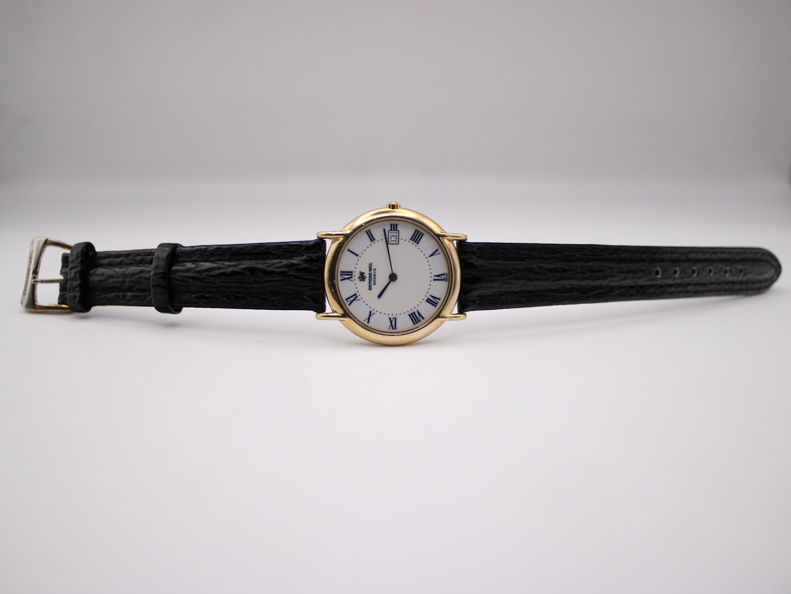 Overhead view of the Raymond Weil watch with its black leather strap fully extended on a white background.