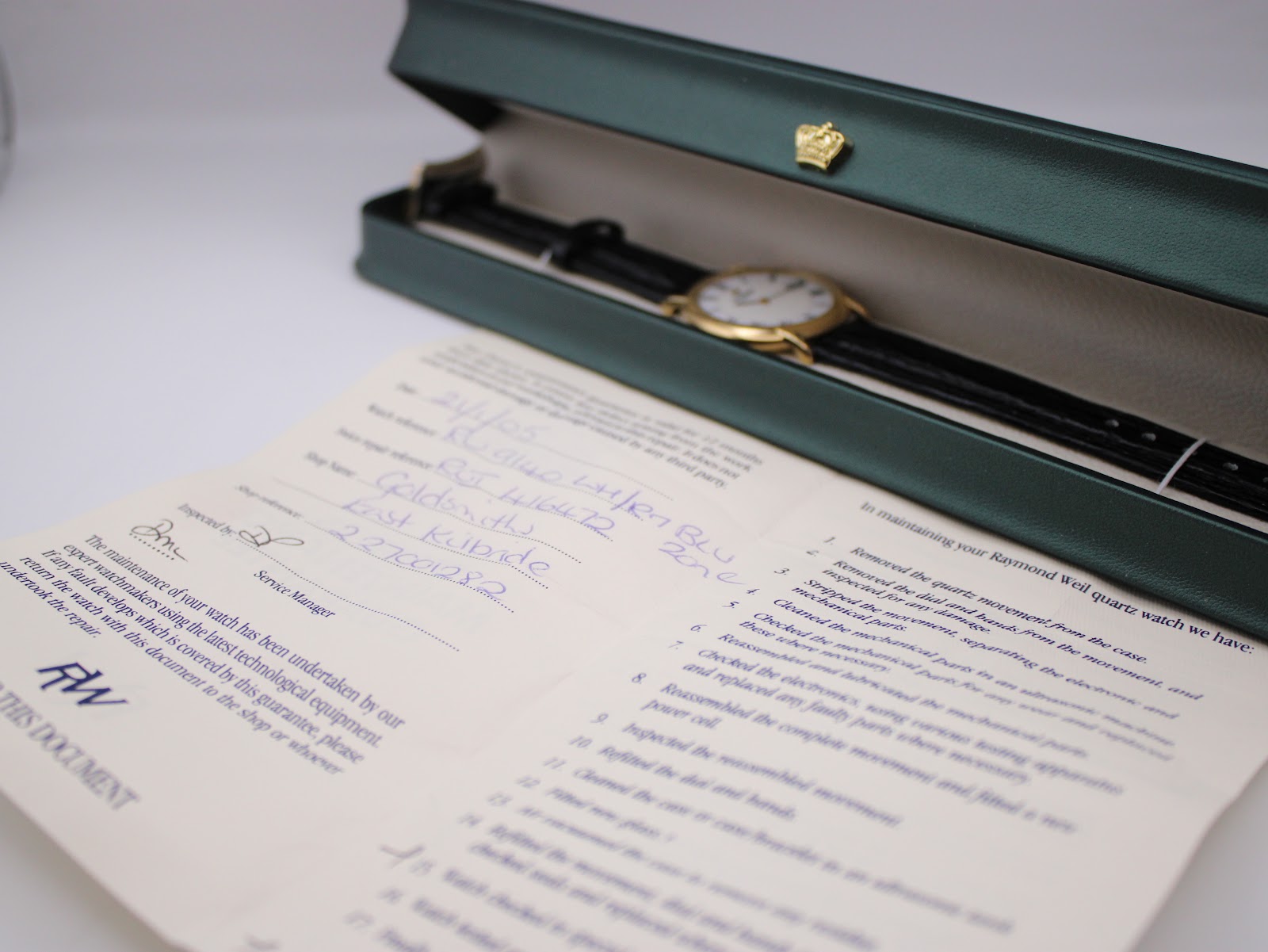 Overhead view of the watch inside a green presentation box, with the maintenance guarantee booklet showing a hand-filled service record in the foreground.