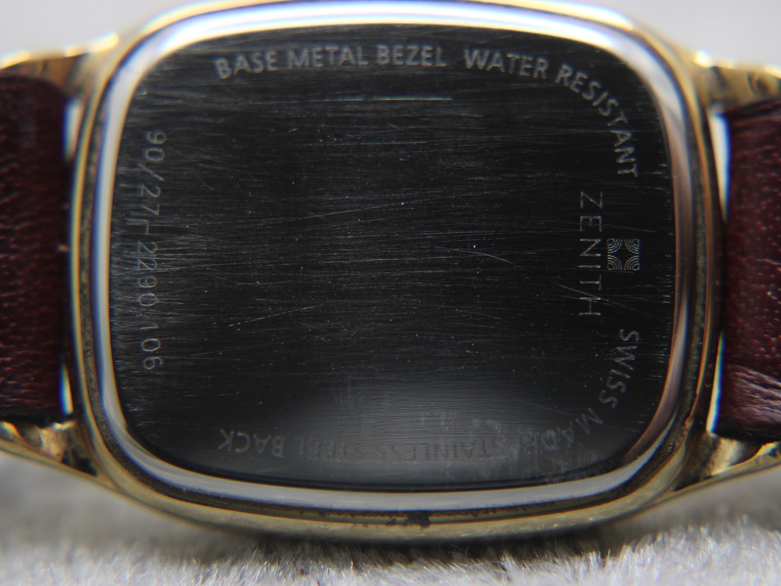 Close-up of the Zenith watch case back, showing scratches and 'base metal bezel water resistant stainless steel back' engravings.