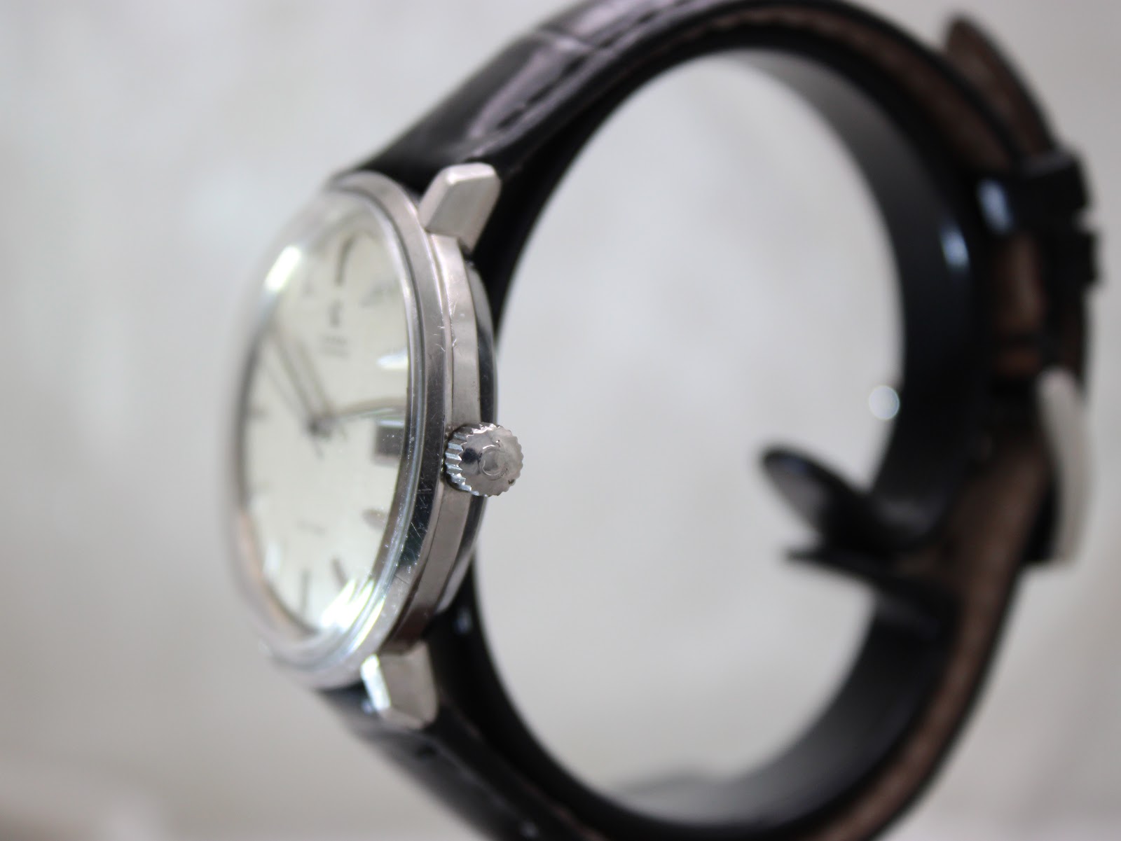 Angled side view of the Omega De Ville watch, highlighting the polished stainless steel case, domed crystal, and fluted crown.