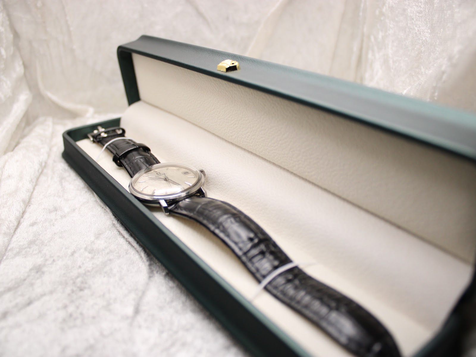 The Omega De Ville watch nestled within a dark green, non-original presentation box with a cream interior.