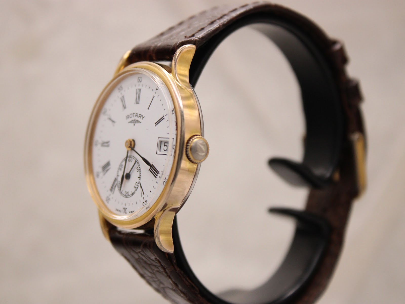 Side view of the Rotary watch on a black display stand, showing the gold-tone crown and case profile.