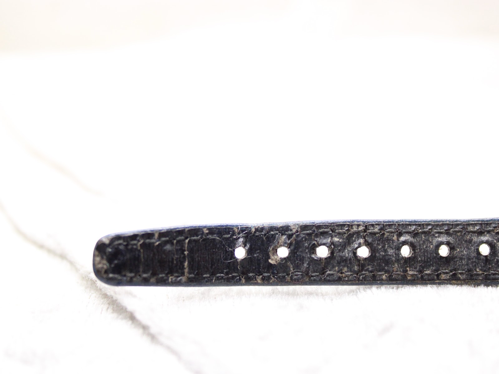 Close-up of the end of the blue perforated leather strap, showing wear and perforations.