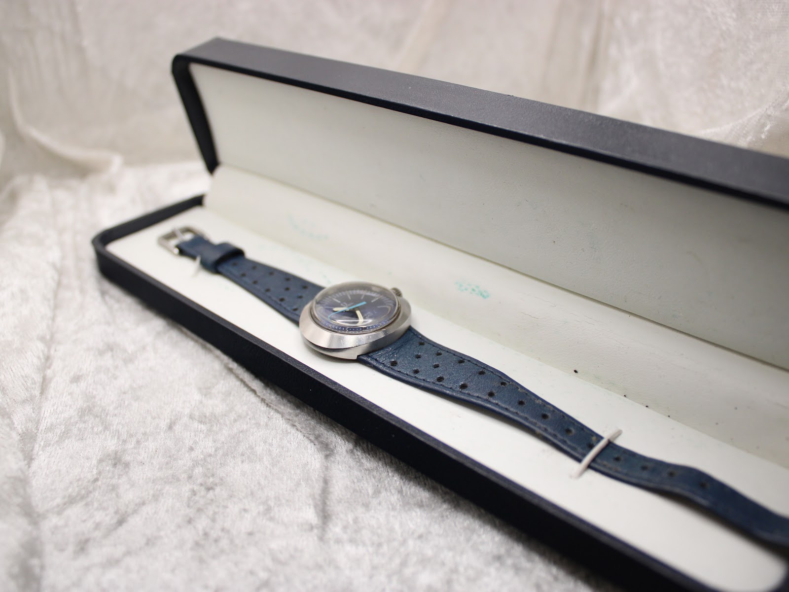 The Omega Genève Dynamic watch resting inside a black presentation box, showing the blue dial and strap.
