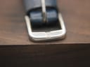 Close-up of the polished stainless steel buckle on the blue perforated strap, clearly featuring the embossed Omega logo.
