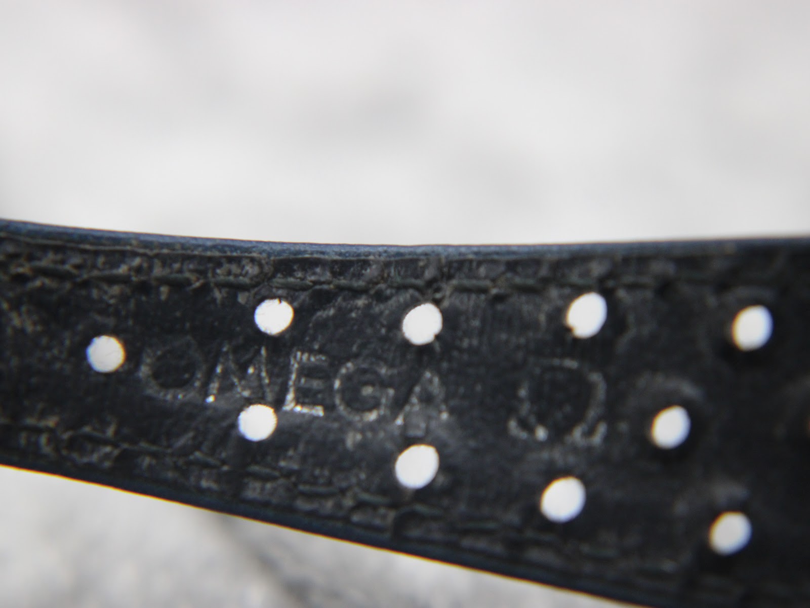 Close-up of the blue perforated leather strap, showing the embossed "OMEGA" logo and strap holes.
