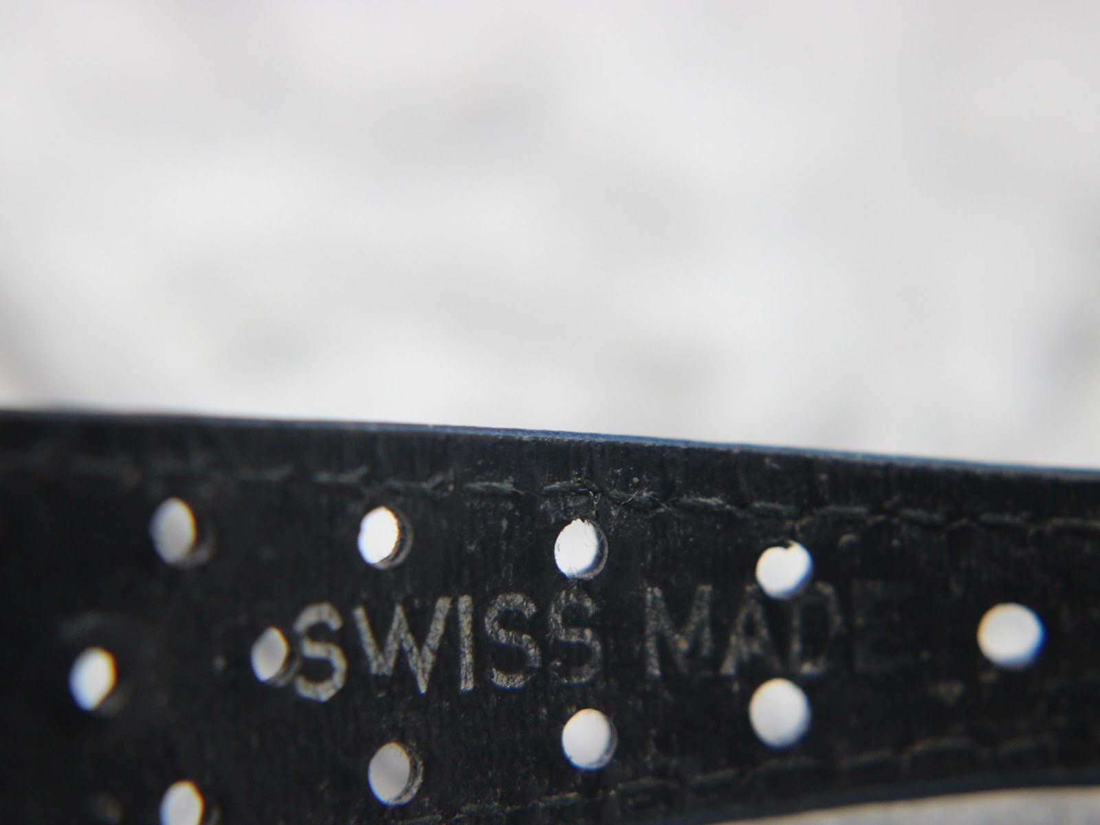 Close-up of the blue perforated leather strap, showing the embossed "SWISS MADE" text and strap holes.