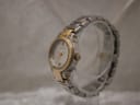 Angled side view of the Gucci 8900L watch on a clear display stand, highlighting the gold-tone crown and bracelet links.