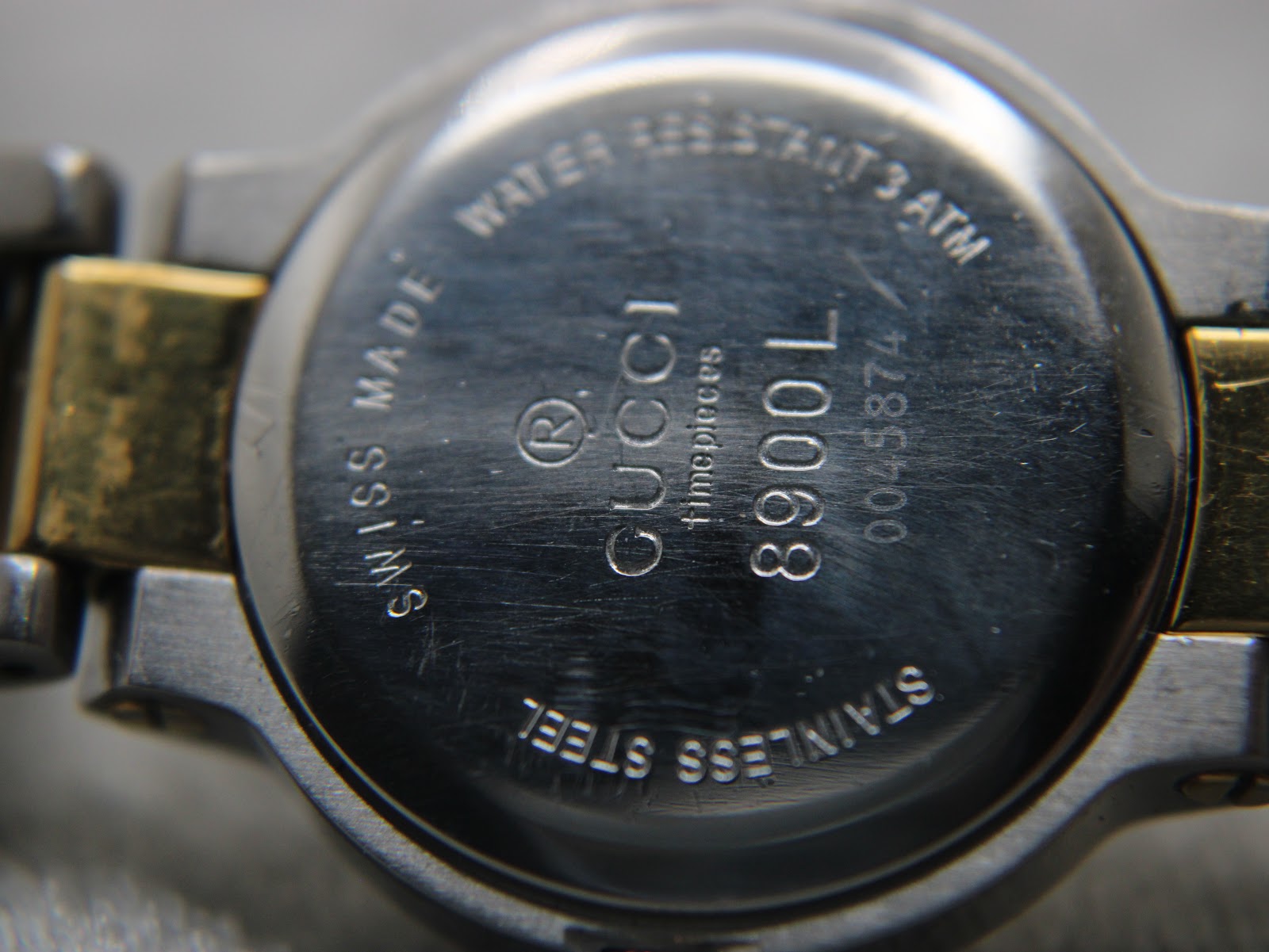 Close-up of the watch's brushed stainless steel case back, engraved with "Gucci Timepieces 8900L", "Swiss Made", and "Water Resistant 3 ATM".
