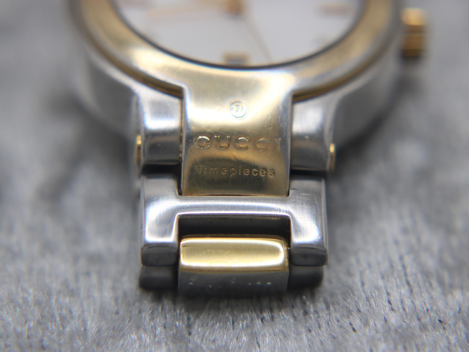 Close-up of the bracelet attachment to the case, displaying the "Gucci Timepieces" engraving on the gold-tone link.