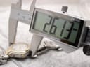 A digital caliper precisely measuring the watch case diameter at 26.13 mm, excluding the crown.