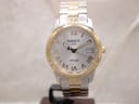 Front view of Tissot PR 100 two-tone watch with silver sunburst dial and gold Roman numerals, on a display stand.