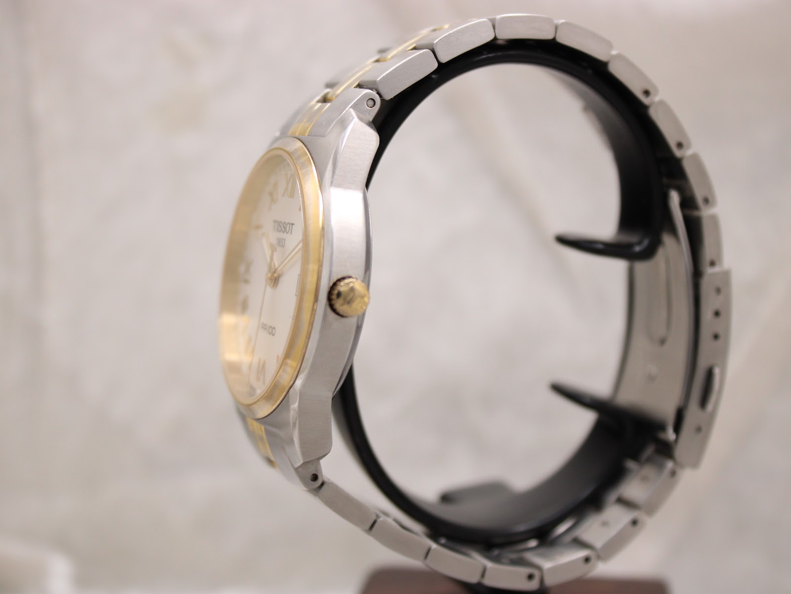 Side view of the Tissot PR 100 watch on a display stand, showing the case profile and two-tone bracelet.