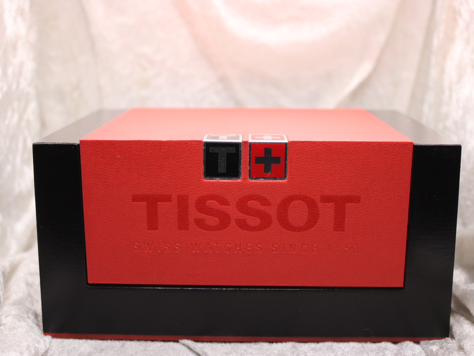 Top view of the closed Tissot watch presentation box in red and black with the brand logo.