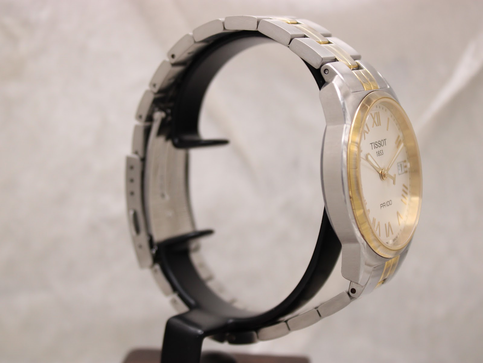 Angled side view of the Tissot PR 100 watch on a display stand, highlighting the bracelet and case.