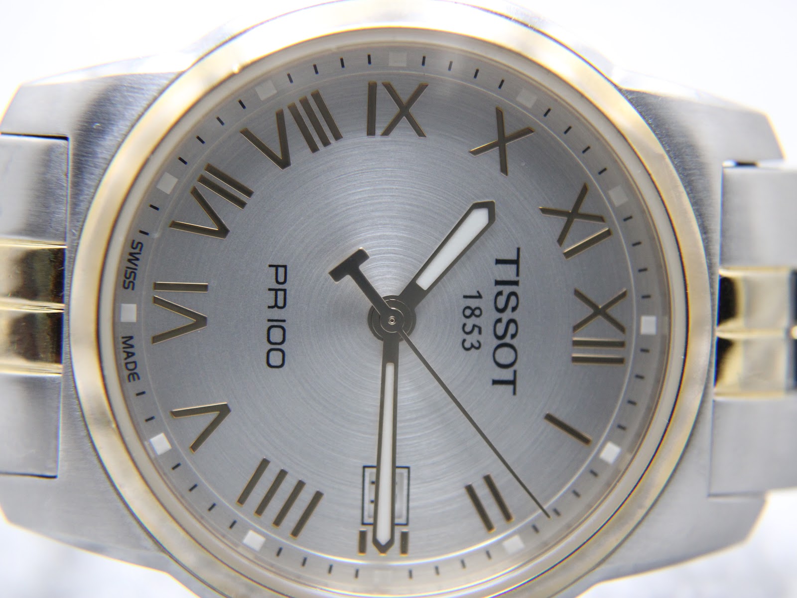 Extreme close-up of the silver sunburst dial with applied gold Roman numerals and the date window at 3 o'clock.