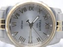 Extreme close-up of the silver sunburst dial with applied gold Roman numerals and the date window at 3 o'clock.