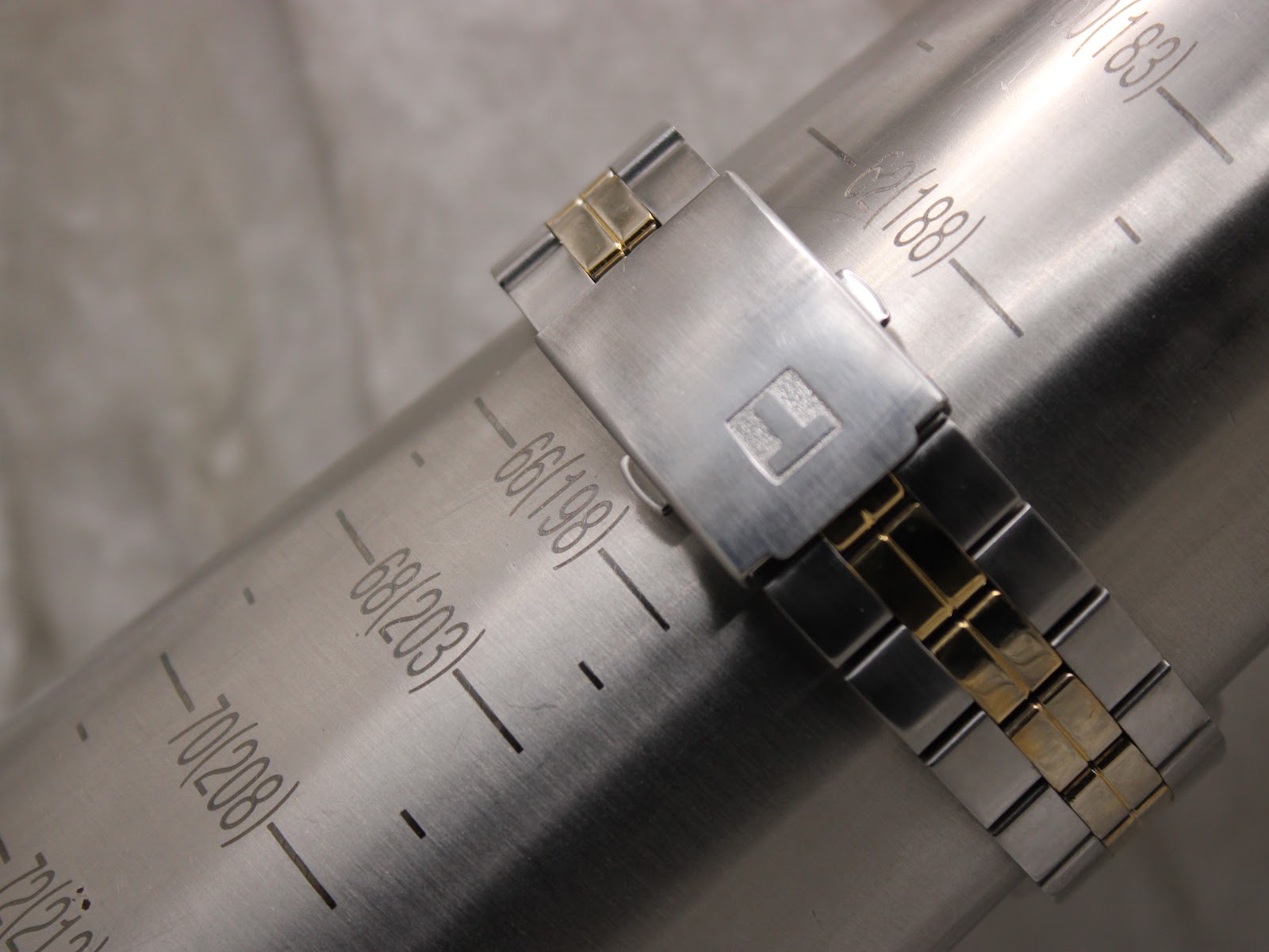The Tissot PR 100 bracelet clasp on a wrist sizing gauge, showing it fits approximately 198mm (66).