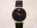 Front view of gold-plated Movado Museum watch with black dial and gold dot on a textured background.