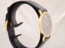 Angled side view of the Movado Museum watch, showing the gold-plated case and black leather strap.
