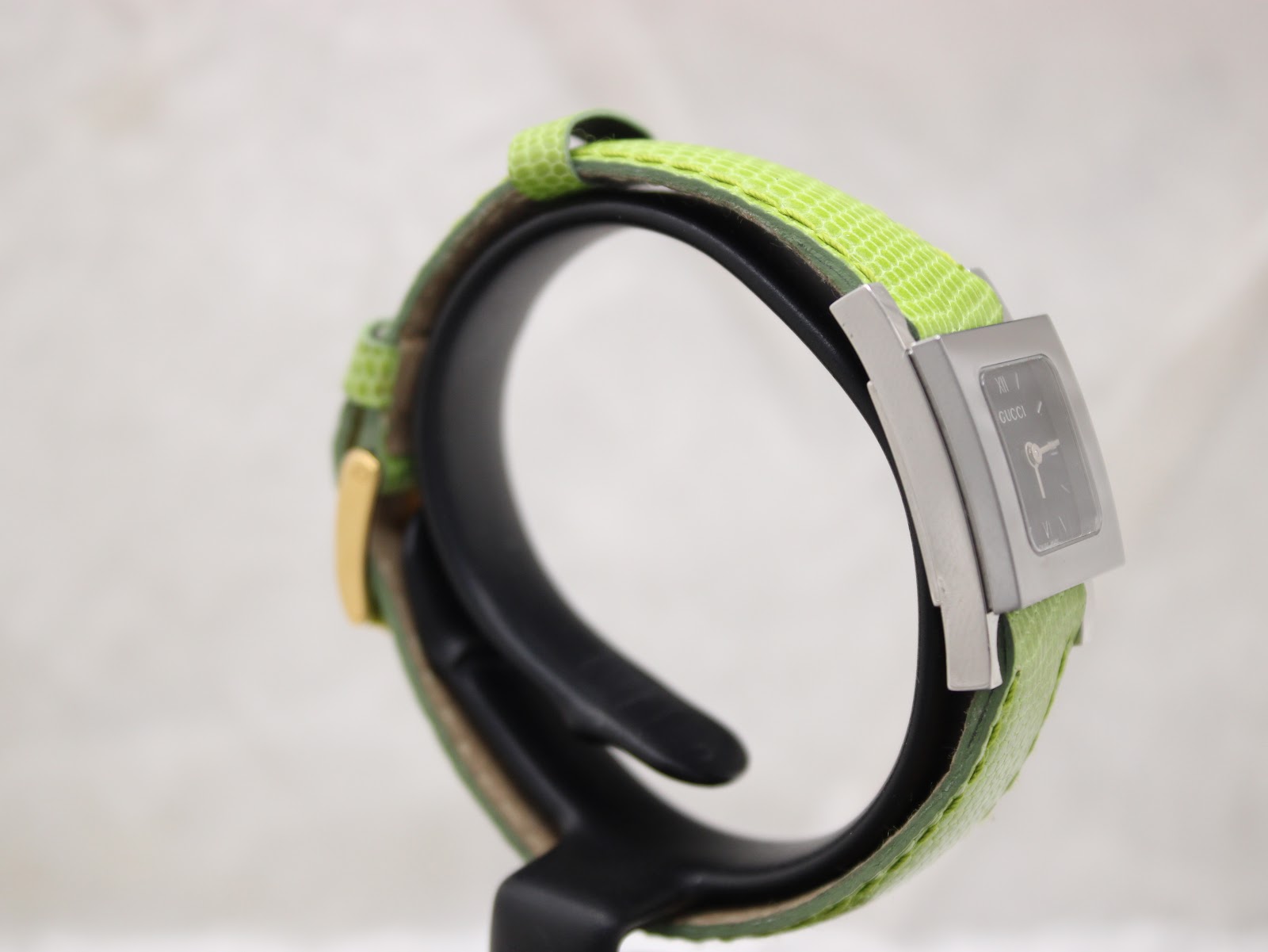 Oblique side view of the Gucci 7900P watch, showing the sleek stainless steel case design and the texture of the green leather strap.