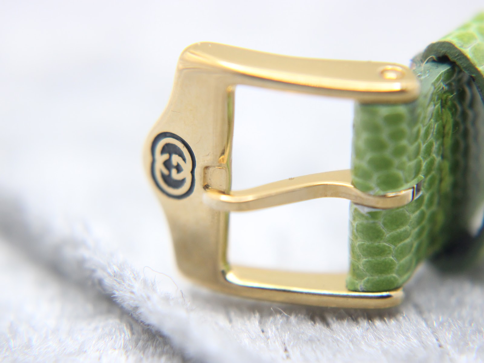 Close-up of the gold-tone buckle of the Gucci watch, featuring the engraved interlocked Gs Gucci logo.