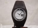 Front view of Gucci 104 watch on a stand, showing white dial with silver G-design case and dark brown leather strap.