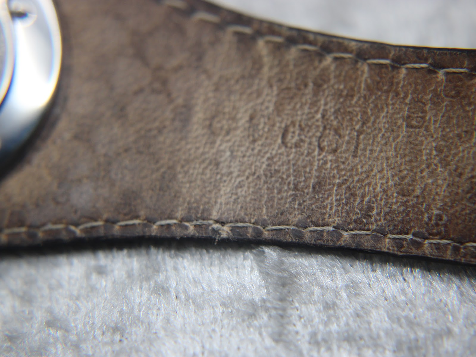 Close-up of the textured dark brown leather strap near the case, showing stitch detail and minor wear.